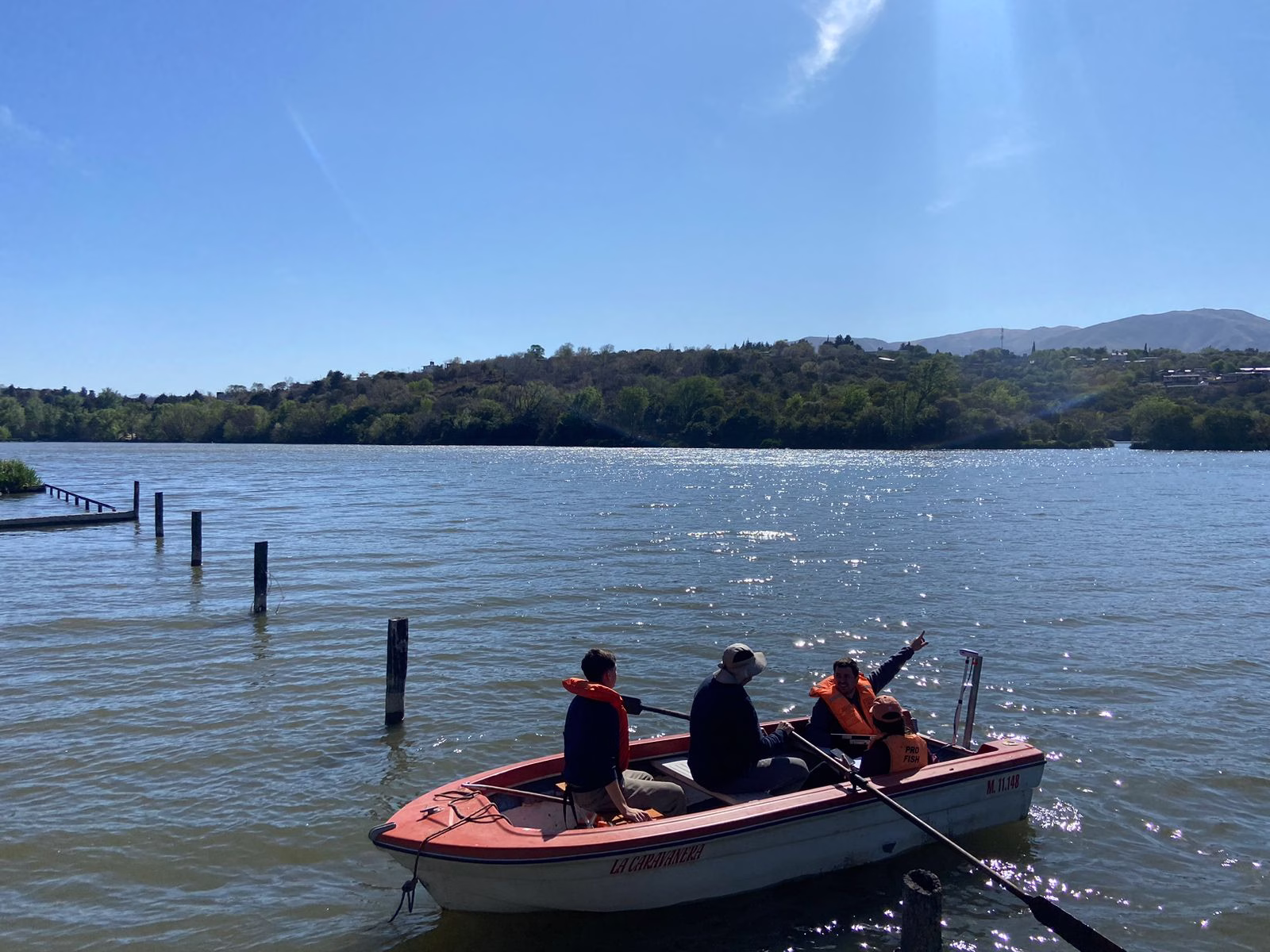 Ingenieros de Geodex con chalecos salvavidas a bordo de un bote a remos en el lago. Uno de ellos señala un punto de interés en la costa mientras transportan equipamiento de medición batimétrica